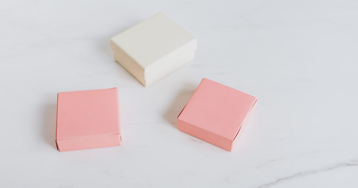 Three small blank gift boxes, two pink and one cream, arranged on a white marble surface
