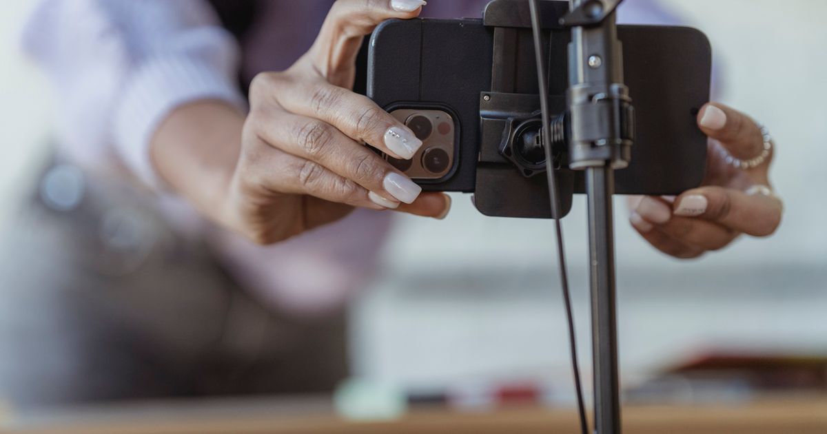 Close-up of a person's hands mounting a smartphone into a clamp on a small tripod on a desk in a bright room