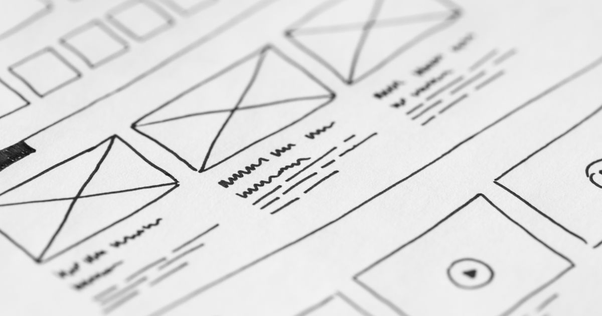 A hand-drawn website wireframe sketch on paper, showing boxes and placeholder content blocks for a page layout